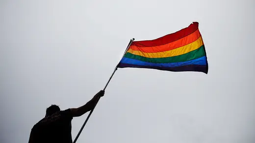 Silhouetted person waves rainbow pride flag.